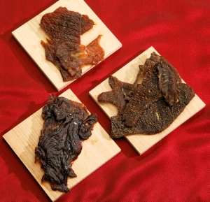 3 different piles of jerky on wooden planks on a red table clothe