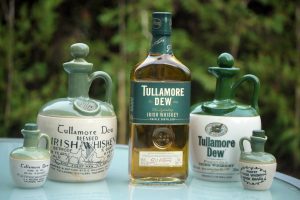 5 different size containers of Tullamore dew Irish Whiskey on a table with trees in the background