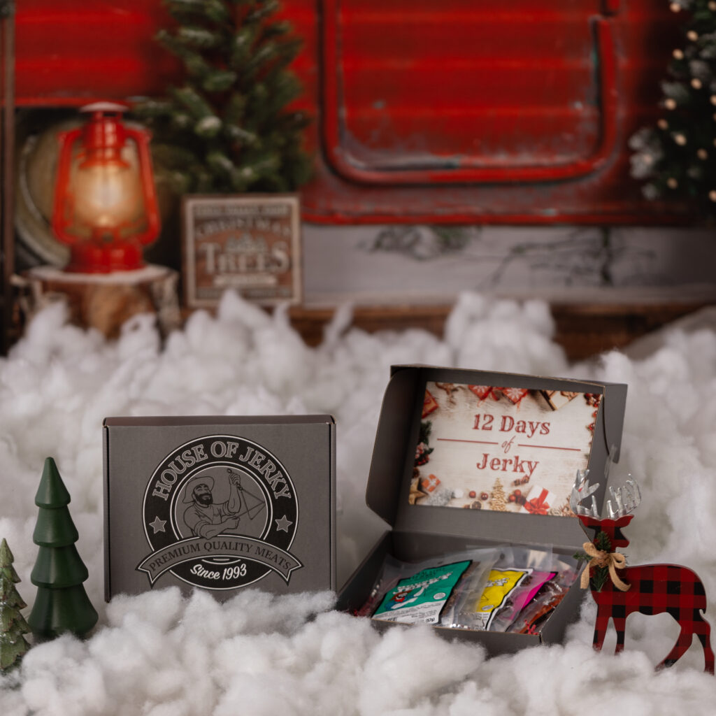 a gray box with the house of jerky logo that has an insert that says 12 days of jerky and has some assorted bags of jerky inside it with a holiday background